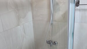 Une cabine de douche fermée par des parois en verre, dotée d’un pommeau de douche à main et d’un robinet fixé au mur.