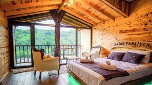 Una habitación de cabaña de madera con una cama, una silla, una mesa y un balcón con vistas a colinas verdes.
