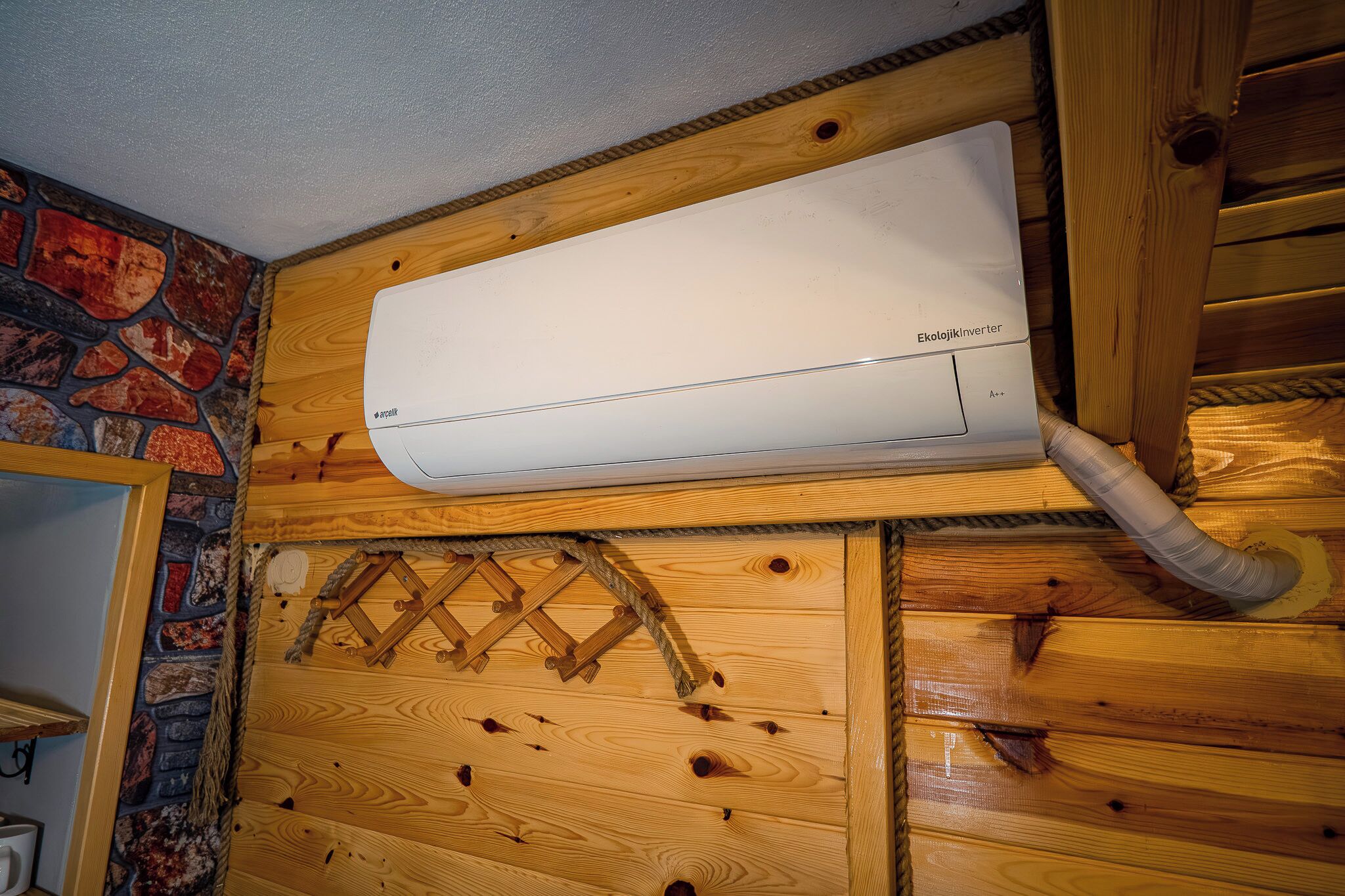 A white air conditioning unit mounted on a wooden wall with a stone accent.