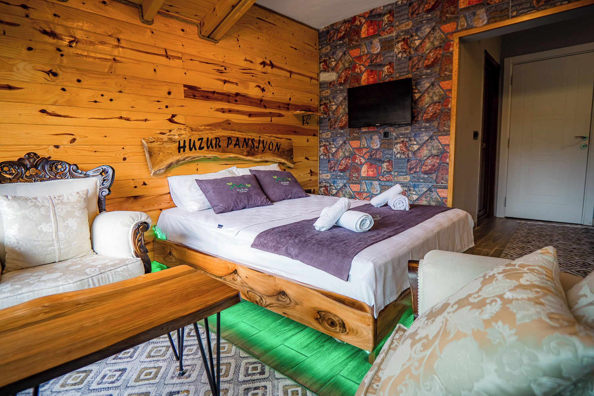A wooden-paneled room with a bed, a sofa, and a television mounted on the wall.