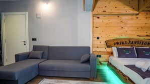 Una habitación con un sofá gris, una cama con cabecera de madera, una puerta blanca y una pared de madera con un letrero.