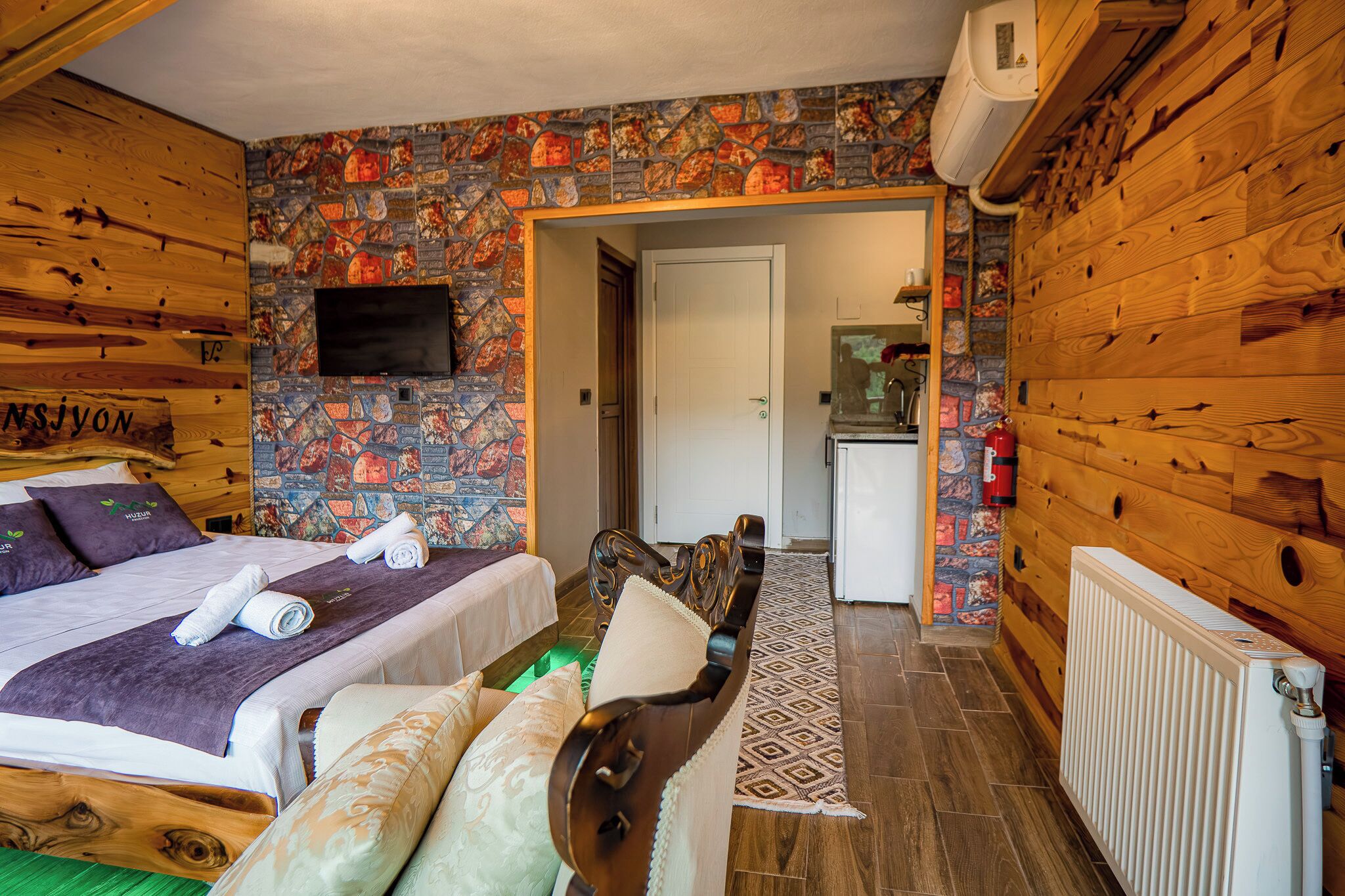 Una habitación de madera con una cama, un banco, un televisor y un papel tapiz estampado.