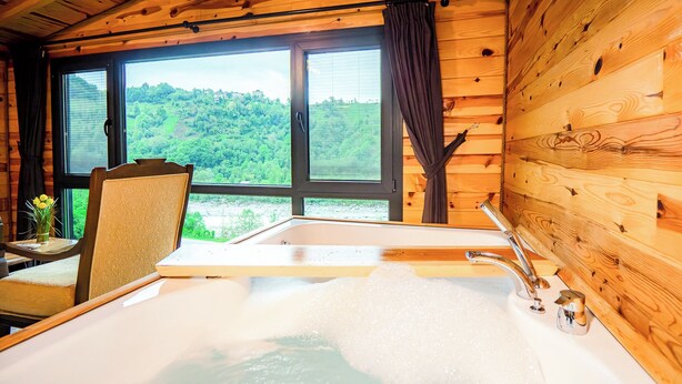 Una cabaña de madera con un ventanal grande, una bañera y una silla.