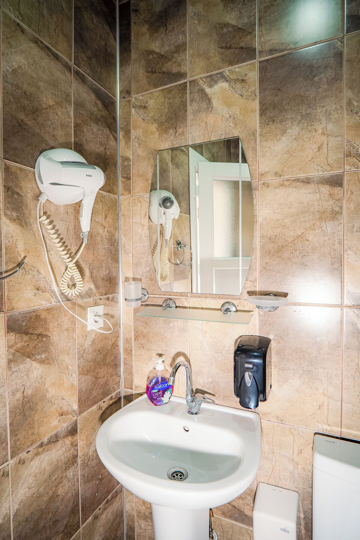 Een badkamer met een wastafel, spiegel, haardroger en zeepdispenser.