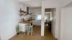 A modern kitchen with white cabinets, a wooden countertop, and a built-in stove. There are two white stools and a potted plant. - El Patio de Tarifa II (tarifa)