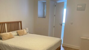 A bedroom with a wooden bed, a hanging light fixture, a door leading to another room, and a radiator on the floor. - El Patio de Tarifa II (tarifa)