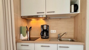 A compact kitchen with white cabinets, a coffee maker, a sink, and a shelf with a plant. - Ferienwohnung in Sellin mit Balkon (Sellin)