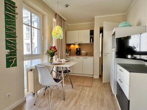 A modern kitchen with white cabinets, a dining table with chairs, a TV, and a window with curtains. - Ferienwohnung in Sellin mit Balkon (Sellin)