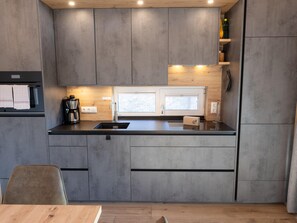 A modern kitchen with a black countertop, grey cabinets, a coffee machine, and a window above the sink. - Ski-in/ski-out Chalet With Beautiful View (Sankt Lambrecht)