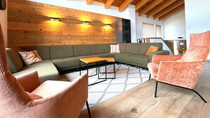 Ein modernes Wohnzimmer mit Holzboden, einem grünen Sofa, einem rosafarbenen Sessel und einer Holzverkleidung.