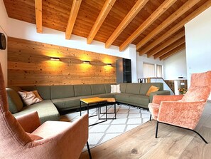 Ein modernes Wohnzimmer mit Holzboden, einem grünen Sofa, einem rosafarbenen Sessel und einer Holzverkleidung.