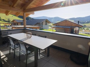 A covered outdoor dining area with a table and chairs, overlooking a mountainous landscape with several buildings. - Ski-in/ski-out Chalet With Beautiful View (Sankt Lambrecht)