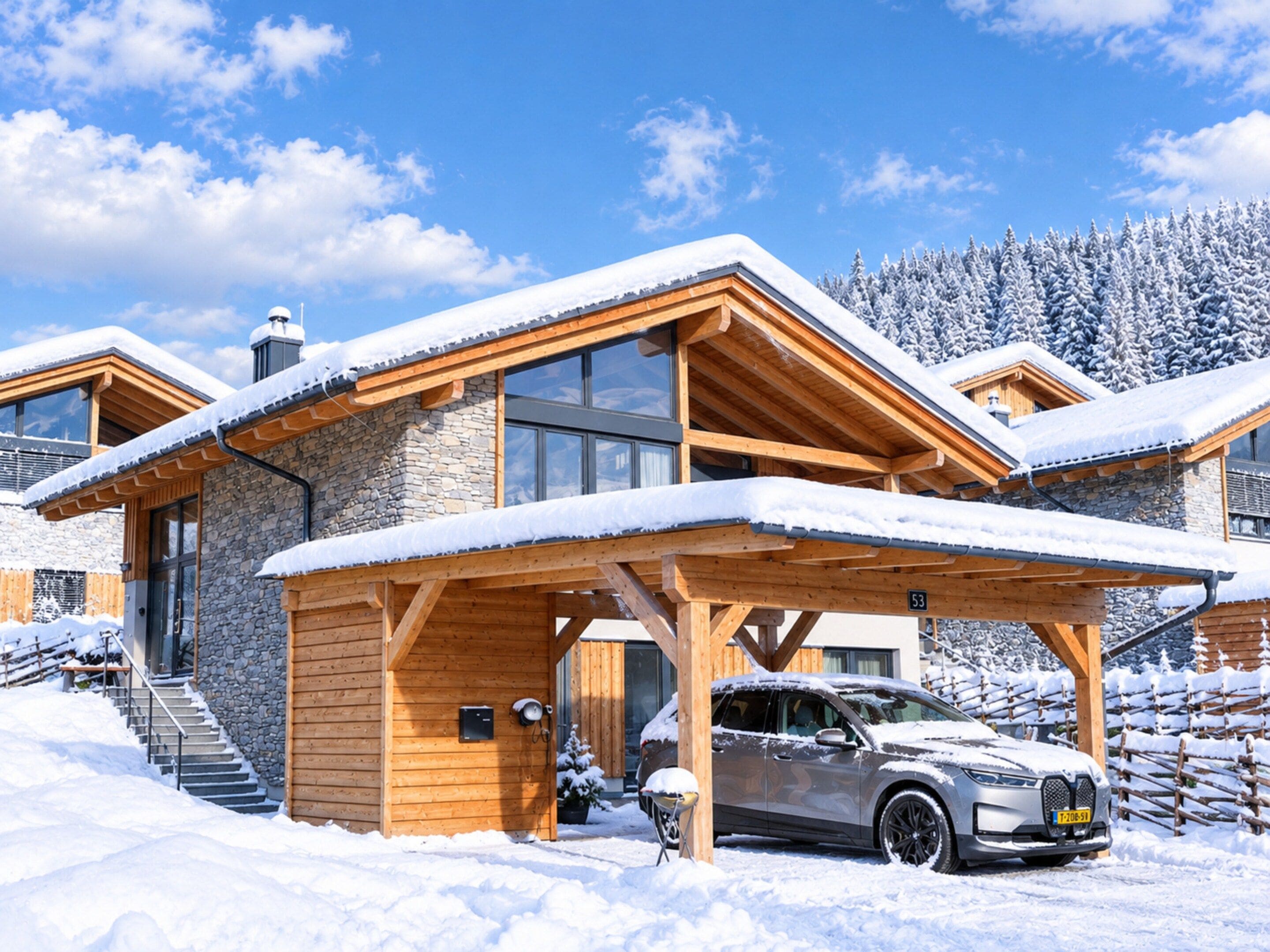A modern wooden house with a car parked in front, surrounded by snow.