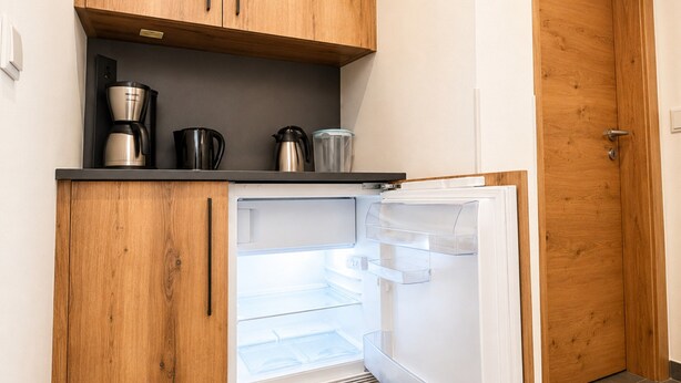 Eine kleine Küche mit Holzausstattung, einer integrierten Kaffeemaschine und einem Kühlschrank.