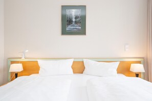 Une chambre d’hôtel avec un lit, deux lampes de chevet, un tableau encadré au mur et un interrupteur près du lit.
