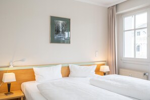 A hotel room with a bed, two bedside tables with lamps, a window with curtains, and a framed picture on the wall. - Ansprechende Ferienwohnung mit Balkon und Badewanne in Sellin (Sellin)