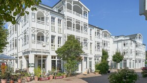 A white building with multiple balconies and a paved area with potted plants and signs. - Ansprechende Ferienwohnung mit Balkon und Badewanne in Sellin (Sellin)