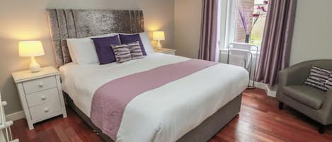 A bedroom with a large bed, two bedside tables, a nightstand, a chair, and a window with curtains.