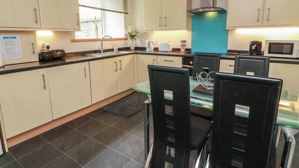 A modern kitchen with light-colored cabinets, a central island, and a dining area with black chairs. - 1 St. Catherines Cottages (Perth)