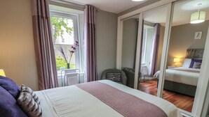 A hotel room with a bed, a chair, a desk, and a view of another room. - 1 St. Catherines Cottages (Perth)