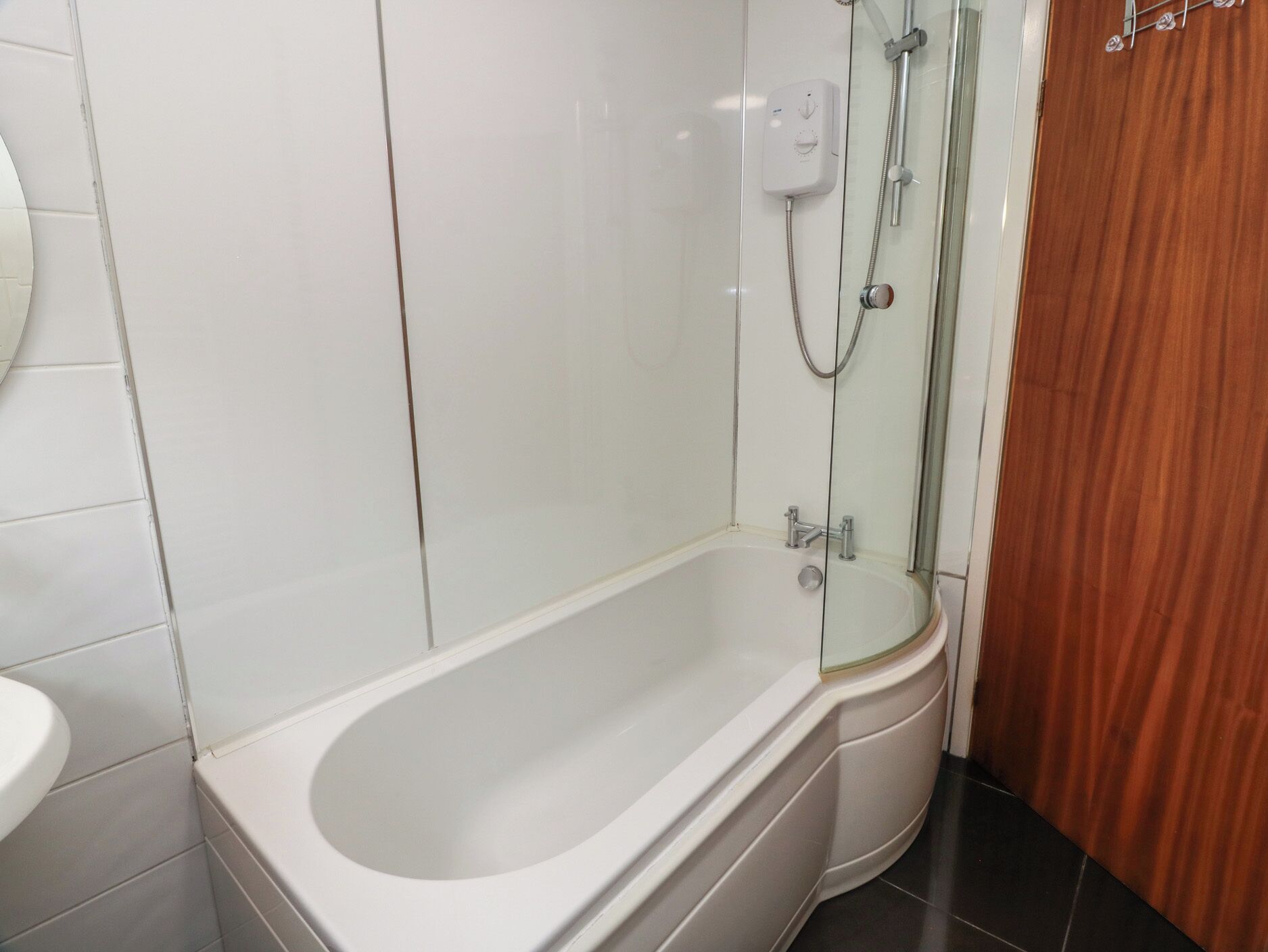 A bathroom with a bathtub, a glass shower enclosure, and a wooden door.