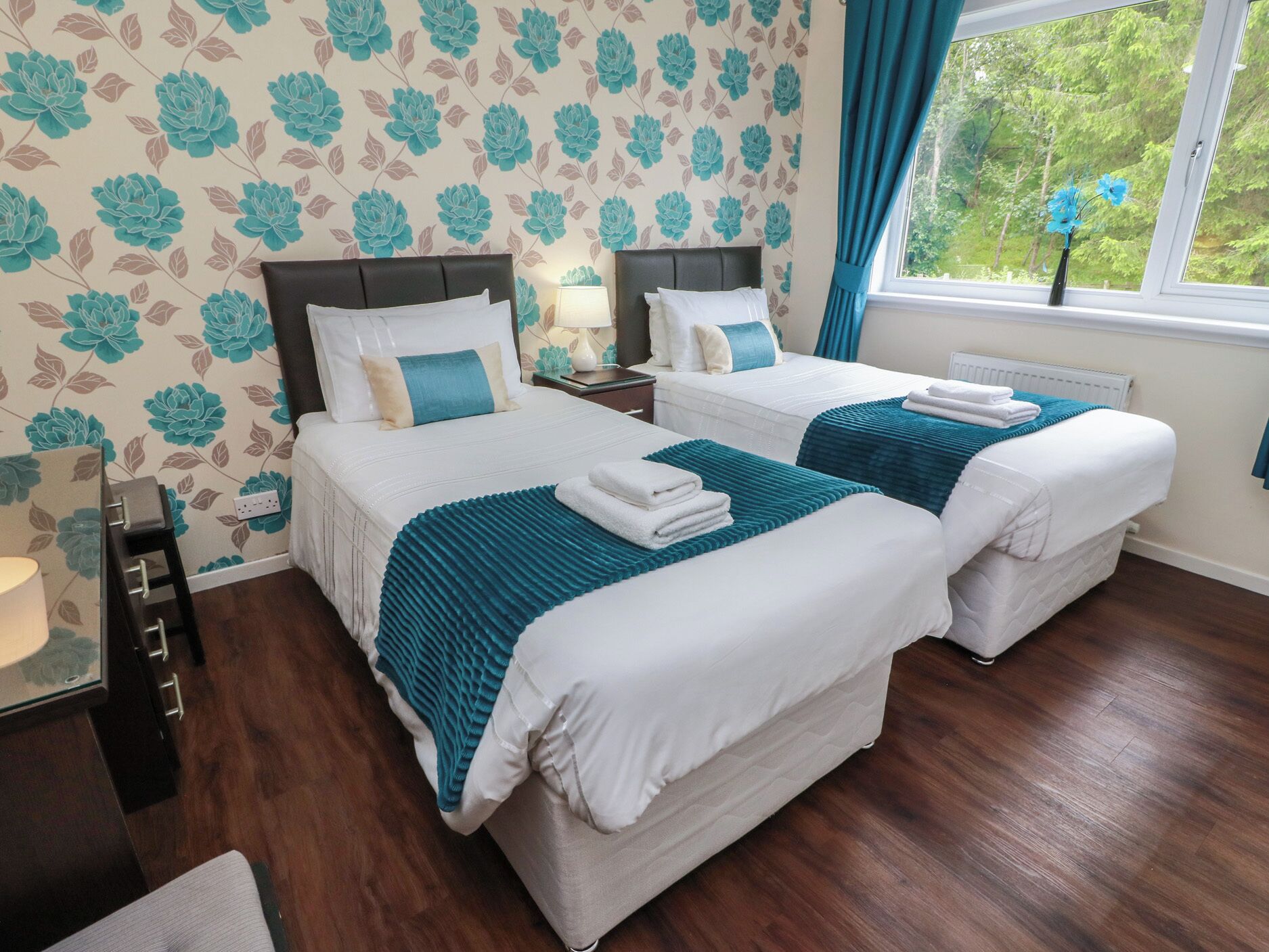 A hotel room with two beds, a nightstand, a dresser, and a window with curtains.