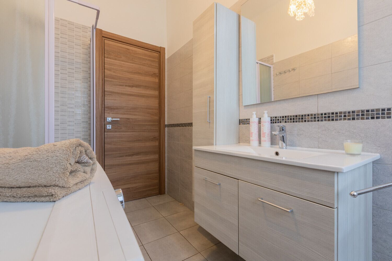 Un baño con puerta de madera, un lavabo blanco con espejo y una toalla en la encimera.