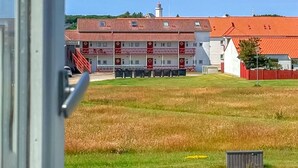 Um edifício com telhado vermelho e fachada branca, um campo gramado na frente e uma escadaria que leva à entrada.