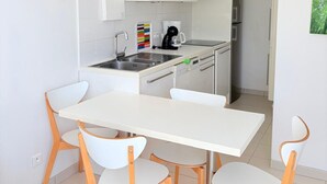 A modern kitchen with white cabinetry, a stainless steel sink, and a dining area with a white table and wooden chairs. - St Cyprien, a sunny interlude by the water (Saint-Cyprien)