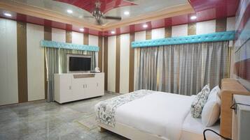 Une chambre à coucher avec un lit, un téléviseur posé sur un meuble, des rideaux et un ventilateur de plafond.