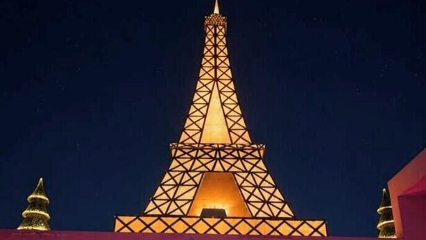Una piscina con una persona en primer plano y un edificio que recuerda a la Torre Eiffel al fondo.