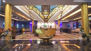 Un hall de hotel con mostrador de recepción, zona de estar y una escalera con barandillas decorativas.