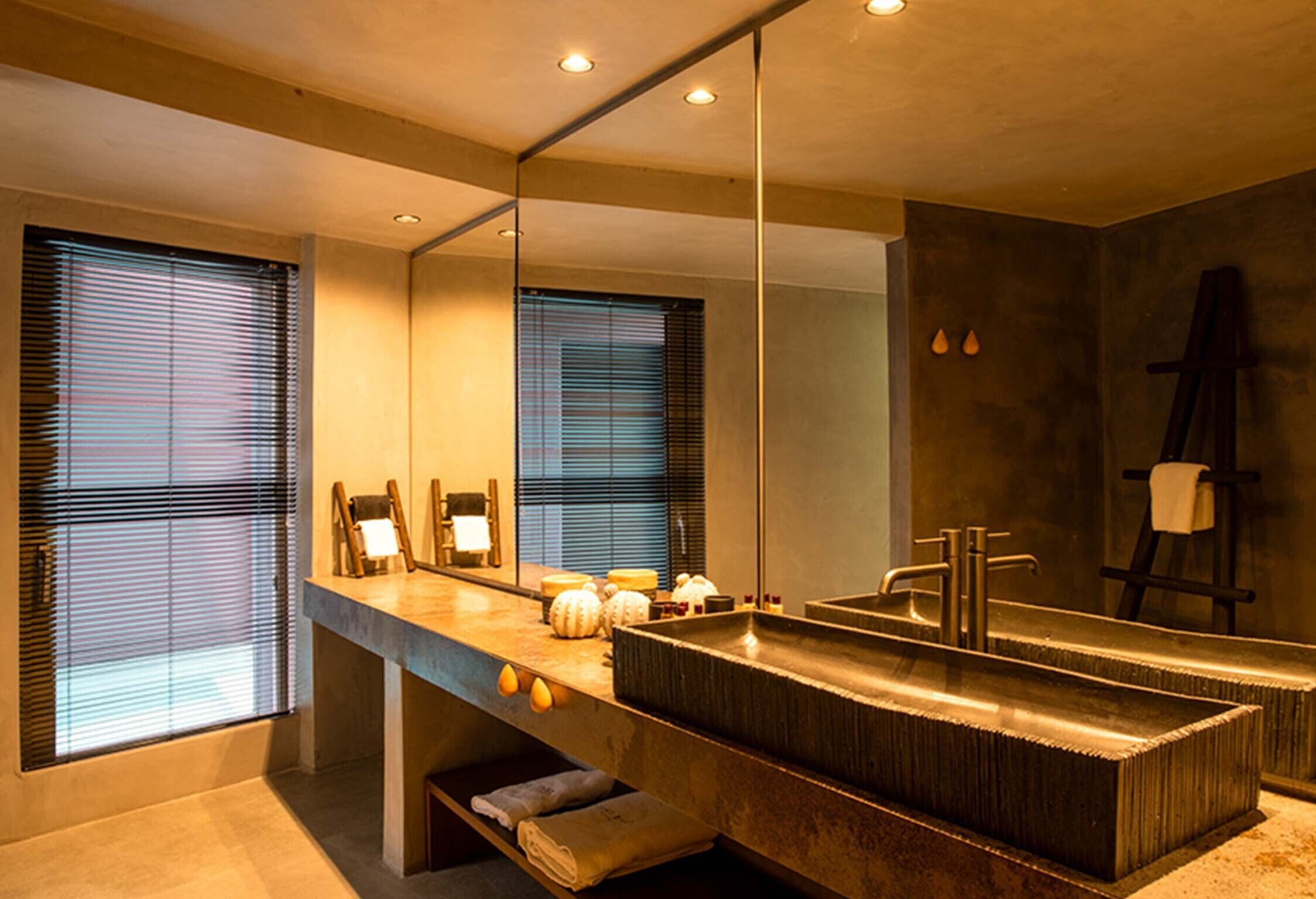 A modern bathroom with a large mirror, a rectangular sink, and a bench.