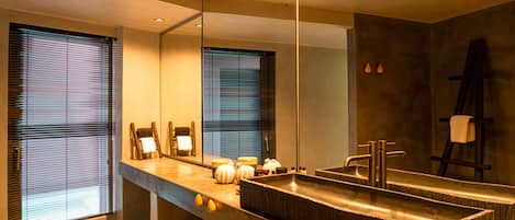 Un baño moderno con un espejo grande, un lavamanos rectangular y un banco.