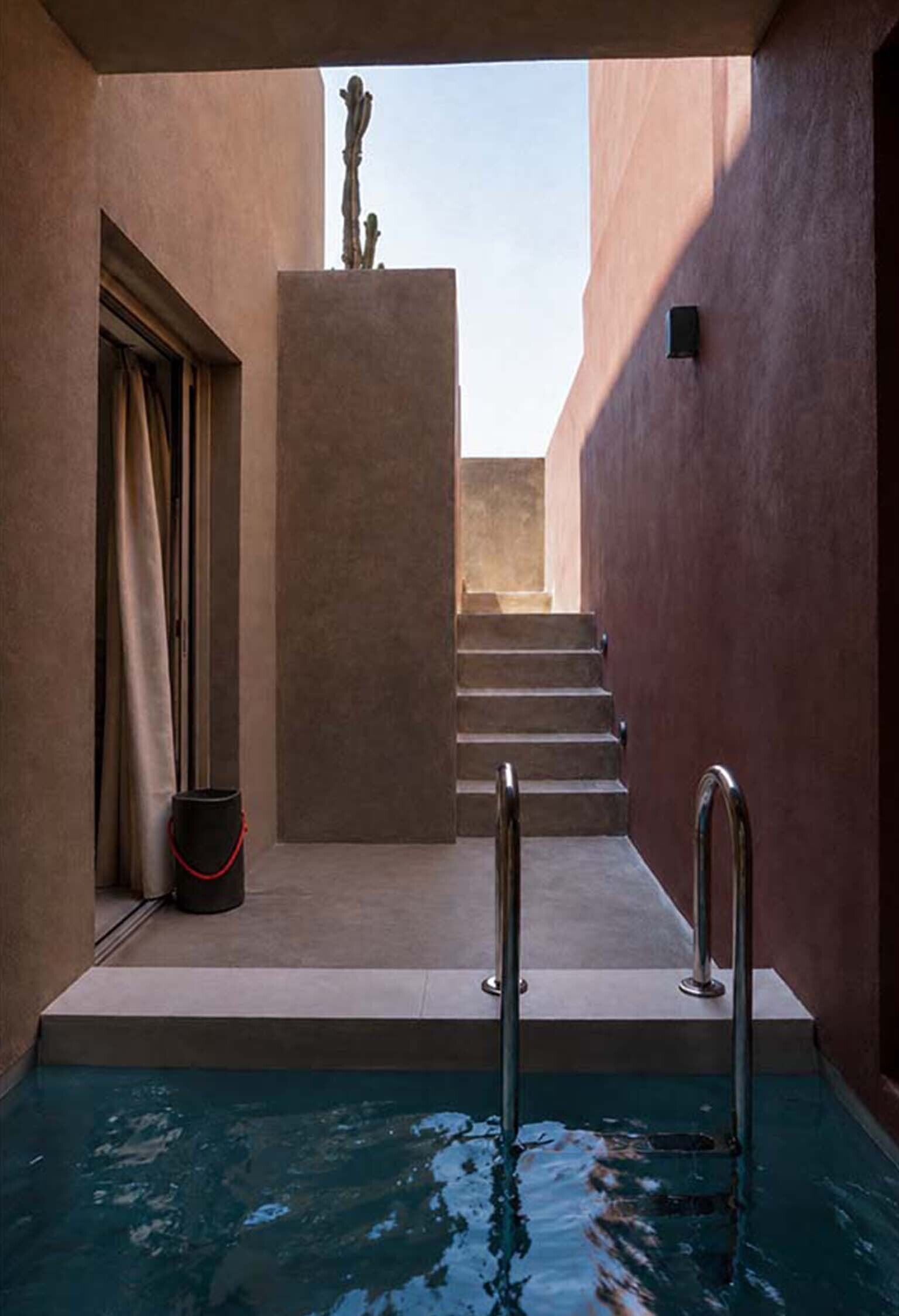 Un área de piscina con una escalera que conduce a un nivel superior, una puerta a la izquierda y una pequeña estatua en la pared.
