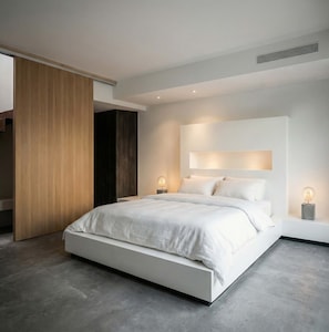 A modern bedroom with a large bed, a wooden wardrobe, and a bedside table with a lamp. - Serenity Villa, Anzo Villas (Thira - Santorini)