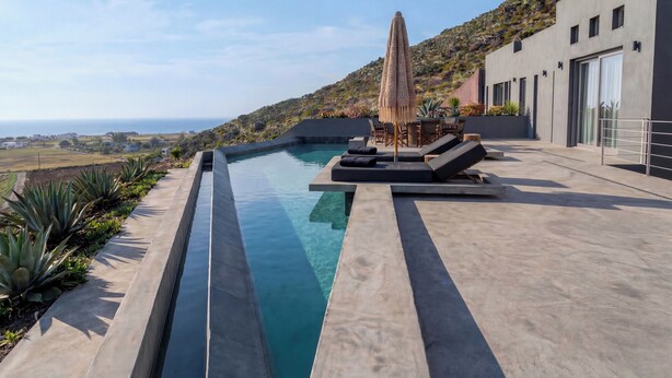 Ein moderner Poolbereich im Freien mit freiem Blick auf den Ozean, eine Lounge mit Sitzgelegenheiten und eine Hügelkulisse.