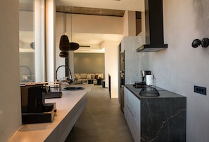 A modern kitchen with a marble countertop, a built-in stove, and a black range hood. - Triangle Art Villa, Anzo Villas (Thira - Santorini)