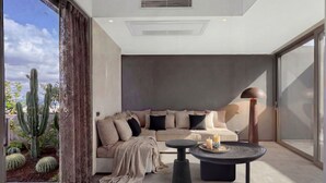 Ein modernes Wohnzimmer mit einer Couch, einem Couchtisch und einem großen Fenster mit Blick auf einen mit Kakteen bepflanzten Garten.