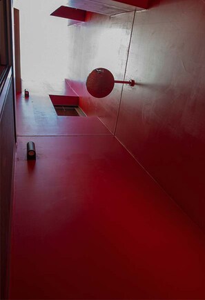 Um interior vermelho com um objeto circular pendurado na parede e uma pequena mesa com uma garrafa.