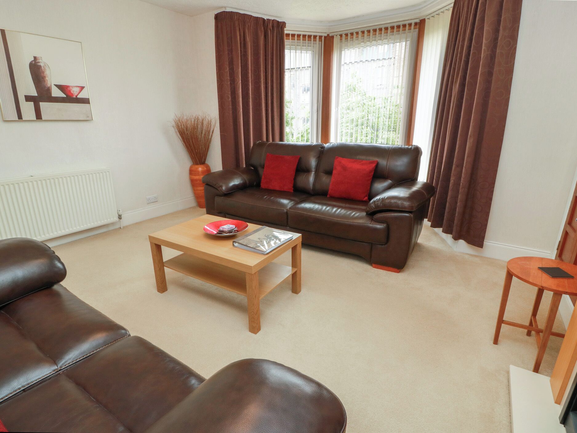 A living room with a brown leather sofa, a wooden coffee table, and a red vase on a shelf.