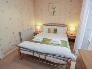 A neatly made bed with a metal frame, two bedside tables with lamps, a radiator, and a wall with a small framed picture. - 2 St. Catherines Cottages (Perth)