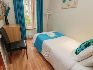 Un dormitorio con cama, escritorio, silla, ventana con cortinas y radiador fijado a la pared.