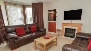 Ein Wohnzimmer mit braunem Ledersofa, einem Holztisch, einem an der Wand befestigten Fernseher und einem Kamin.