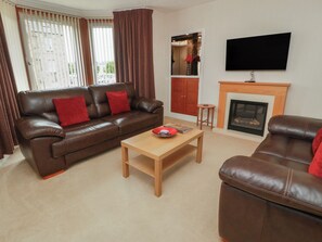 A living room with a brown leather sofa, a wooden coffee table, a television mounted on the wall, and a fireplace. - 2 St. Catherines Cottages (Perth)