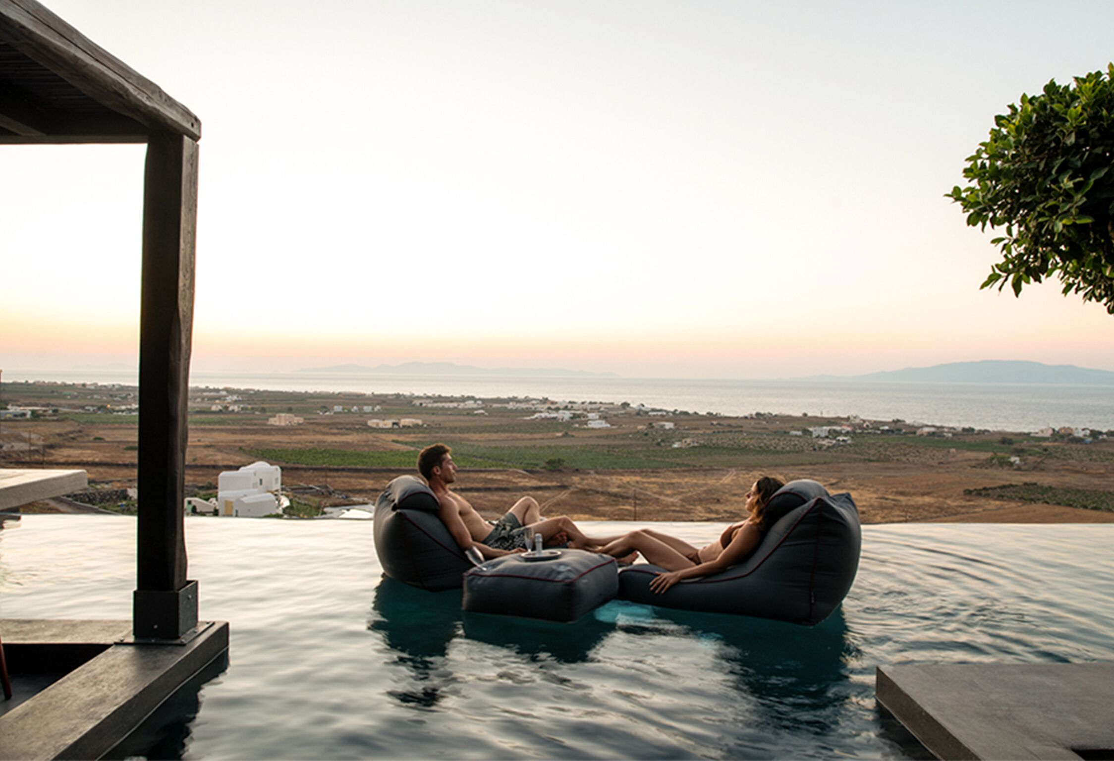 A couple relaxing on an infinity pool with a view of the landscape.