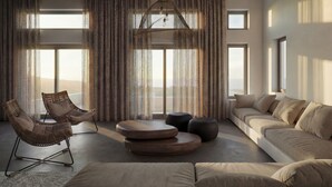 A spacious living room with a large window, a hanging light fixture, a sofa, and two chairs. - Dreamscape Villa, Anzo Villas (Thira - Santorini)