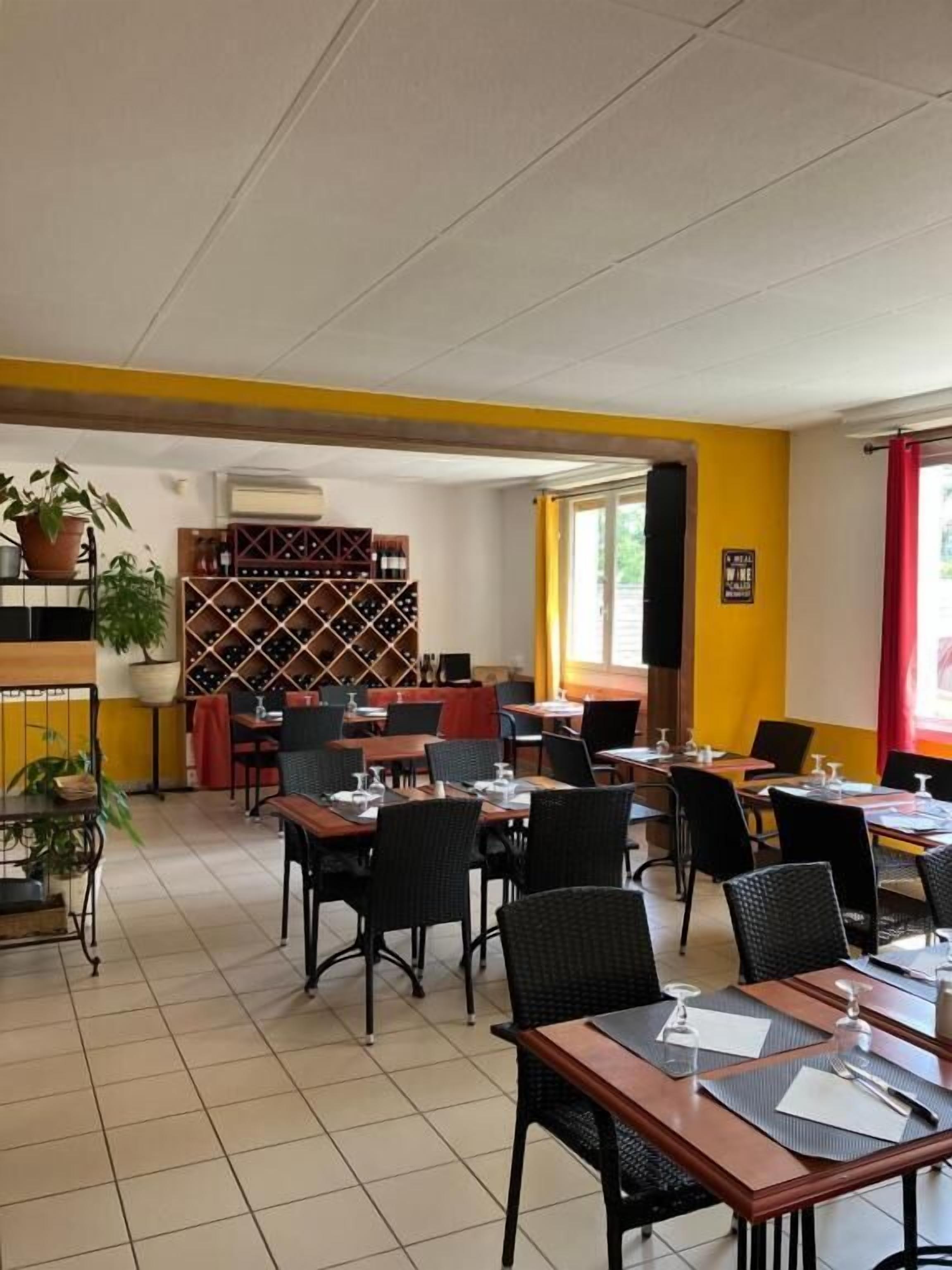 Un restaurante con mesas y sillas, una estantería para vinos y una planta en maceta.