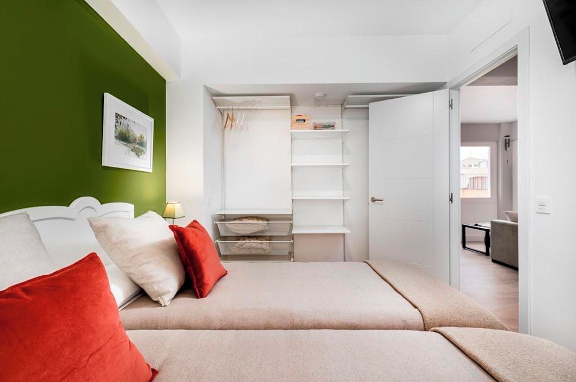 A bedroom with a bed, pillows, a bedside table, a shelf unit, and a green wall.