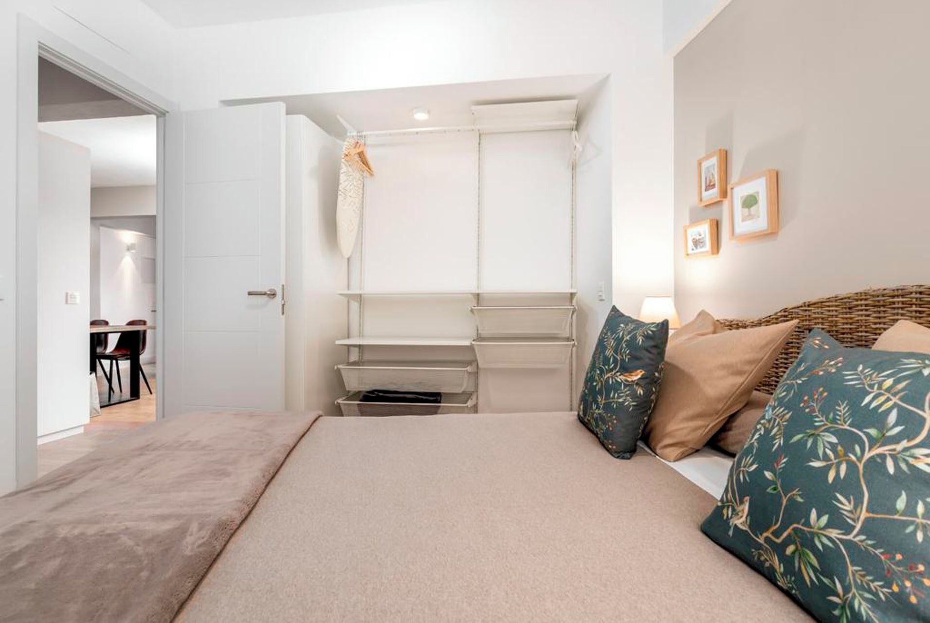 Ein Schlafzimmer mit einem Bett, einem Kleiderschrank, einer Kleiderstange und einem Essbereich, der durch eine offene Tür sichtbar ist.